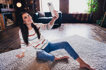 Photo of pretty cute lady dressed striped jumper sitting floor texting selfie modern gadget indoors...