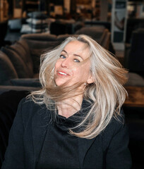 Joyful Silver-Haired Woman in Elegant Black Outfit Enjoying a Lighthearted Moment in a Furniture...
