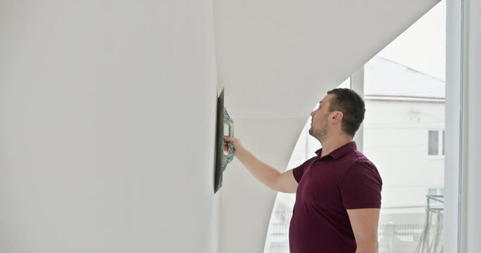 Man painting the walls of a modern, minimalistic apartment. The image depicts a moment of self-repair and renovation, highlighting the trend of DIY home improvement. Tools and paint buckets