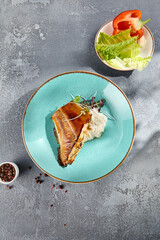 Pan-seared halibut in Unagi sauce with creamy rice served on a turquoise dish, against a textured...