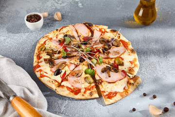 Artisanal pizza topped with ham, mushrooms, olives, and fresh garnishes, served on a textured gray...