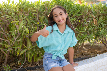 Portrait of happy girl in elementary school age showing thumb up outdoors in green park