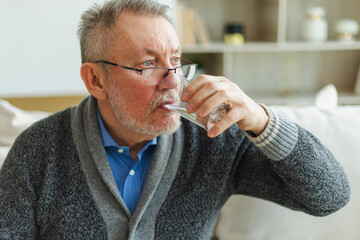 Senior man holding glass drinking fresh water at home. Mature old senior thirsty grandfather takes...