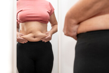 Close-up of woman taking excess fat from her abdomen and looking at herself in the mirror. High quality photo