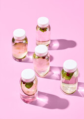 Refreshing detox water with cucumber, cranberries, and mint in reusable bottles on a vibrant pink background. A concept of healthy eating in a modern, minimalist style