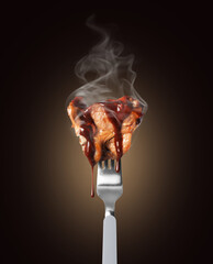 Hot fried beef steak poured with sauce on a fork close up on a black background
