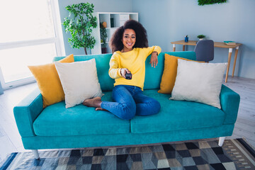 Fototapeta premium Photo of adorable cheerful girl sitting on couch turning on tv watching movie in cozy apartment daylight indoors