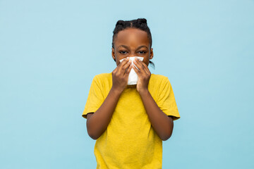 Sick dark- skinned little boy sneezing with handkerchief