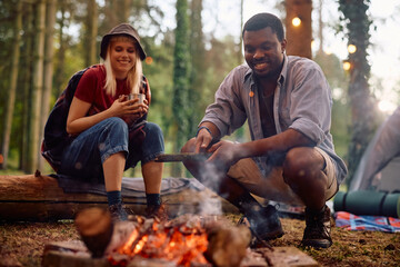 Happy multiracial couple enjoying by bonfire while camping in nature.