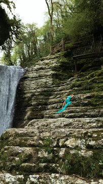 beautiful girl in a long bright fabric poses against the background of a magnificent waterfall among the mountains. 4K vertical video