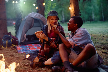 Cheerful couple eating hot dogs while camping in the forest.