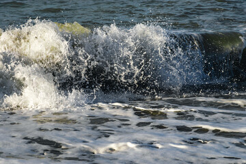 Close-up of a wave on the Black Sea coast. Sea foam of a coastal wave on a sandy beach in close-up. Coastal waves. Selective focus. View of the waves of the Black Sea. Clear wavy sea water.