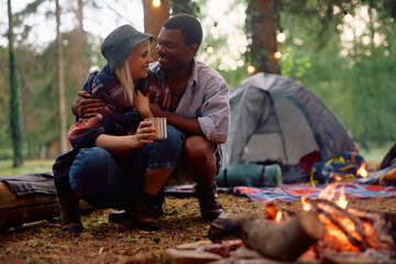 Young happy couple talking while relaxing by campfire in forest.