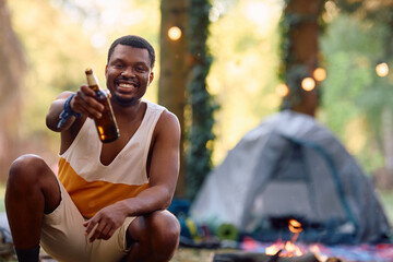Happy black man toasting while camping in nature and looking at camera.
