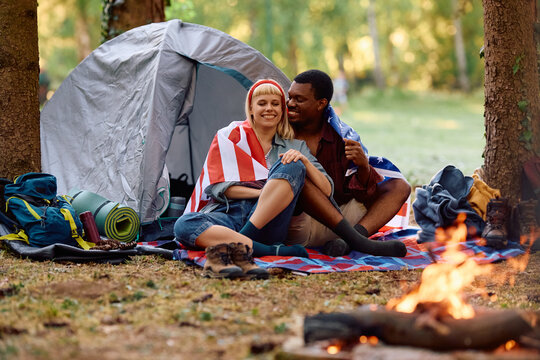 Happy couple relaxing by campfire in woods of America. - Powered by Adobe