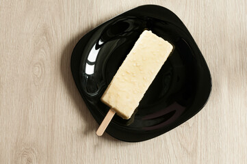 Ice cream on a stick in white chocolate on a black plate. View from a high angle. Daylight