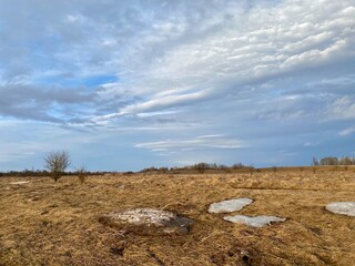 Spring village landscape: cloudy sky, dry grass and large white ice floes on the field