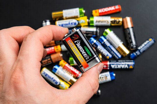 BERLIN , GERMANY - APRIL 14 2024: 9 Volt type alkaline battery in mans hand and AA size batteries on the table.