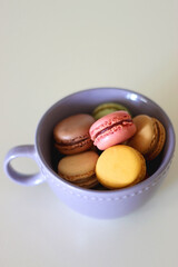 Purple cup filled with pastel macarons on white background. Selective focus.