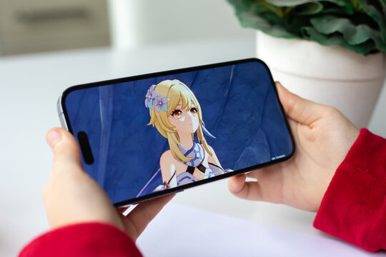 Children hands holding iPhone 15 Pro Max with game Genshin