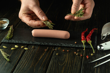 Cooking Munich sausage. The chef hands add fragrant rosemary to the sausage on the kitchen table...