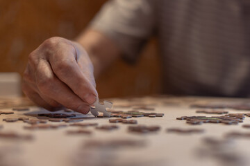 hands working on a puzzle at home,  senior man playing jigsaw puzzle as dementia therapy
