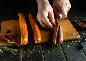 The cook cuts the meat sausage with a knife before frying. Cooking sausages on the kitchen table by...