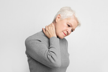 Senior woman with neck pain on grey background