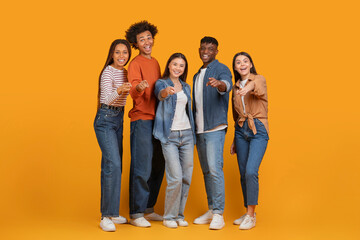 Multiracial friends pointing and laughing on orange background