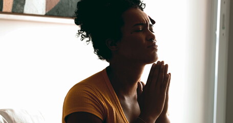 One religious young black woman Praying quietly at home seeking help and support from God with eyes...