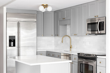 A grey kitchen detail with stainless steel appliances, gold faucet, white marble countertops, and a...