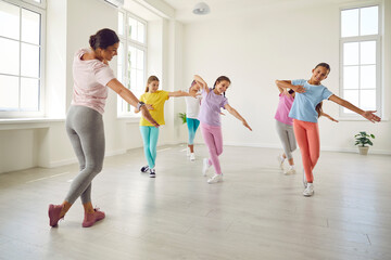 Smiling happy girls training modern dance moves together in studio with female choreographer. Group...