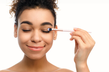 Black lady applying eye makeup with a brush