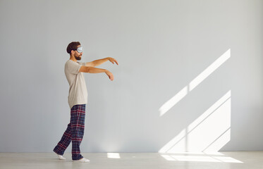 Full length portrait of young sleepwalker man in pajamas suffering from sleepwalking in sleep mask...