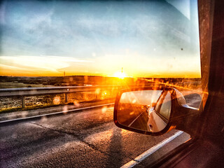 The side mirror of the car and the sun with bright rays behind it and the track on a trip in nature - obrazy, fototapety, plakaty