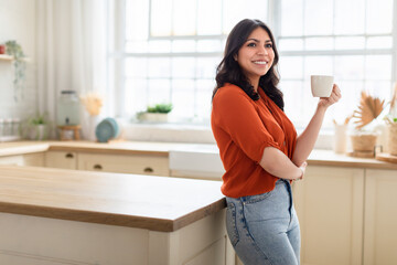 Woman in kitchen with arms crossed holding mug