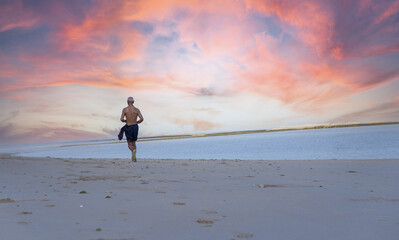 Older man with fit strong body  in sports clothes warm up training run jogging on the beach next to...