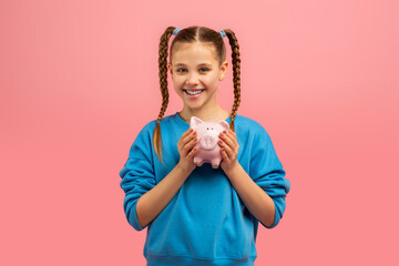 Smiling girl holding a piggy bank on pink background
