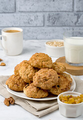 A stack of oatmeal cookies on a plate, raisins, walnuts, a glass of milk, a cup of coffee..