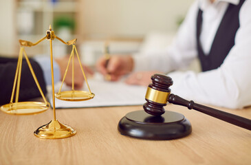 Close up golden scales of justice and dark brown wooden gavel on beige work table at lawyer's...