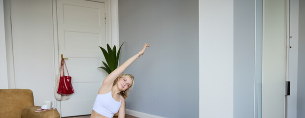 Portrait of young woman personal yoga instructor, recording workout video at home, using digital...