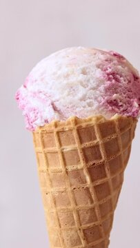 Ice cream cone close-up. Zoom in. Pink Icecream scoop in waffle cone rotated over light background.  Vanilla and strawberry or raspberry flavor Sweet dessert, rotation closeup. 4K