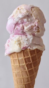 Ice cream cone close-up. Pink Icecream scoop in waffle cone rotated over light background.  Vanilla and strawberry or raspberry flavor Sweet dessert, rotation closeup. 4K