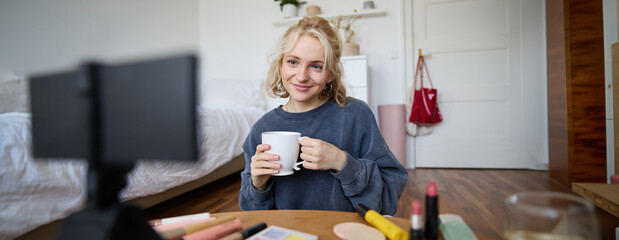 Portrait of cute blond woman, video content maker, vlogger recording on digital camera in bedroom,...