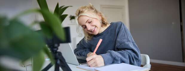 Portrait of young woman, lifestyle blogger, recording video of herself, making notes, writing in...