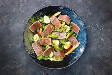 Appetizing salad nicoise in a deep beautiful plate on a dark background