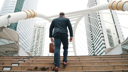 Smart caucasian businessman walking up stairs surrounded by urban view. Back view of ambitious...