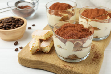 Delicious tiramisu in glasses, cookies and coffee beans on white table, closeup