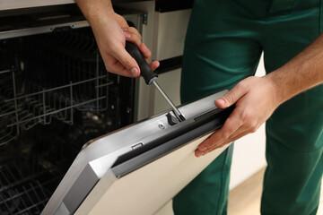 Serviceman repairing dishwasher door with screwdriver indoors, closeup