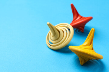 Many colorful spinning tops on light blue background, closeup. Space for text